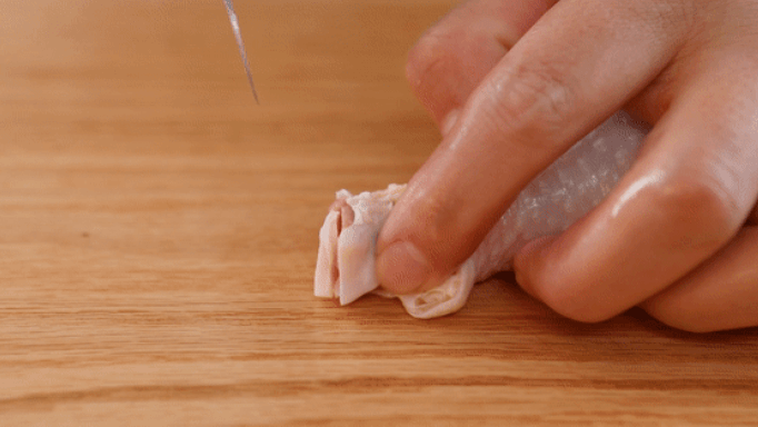 The chicken drumstick is cut at the bone joint with a knife.